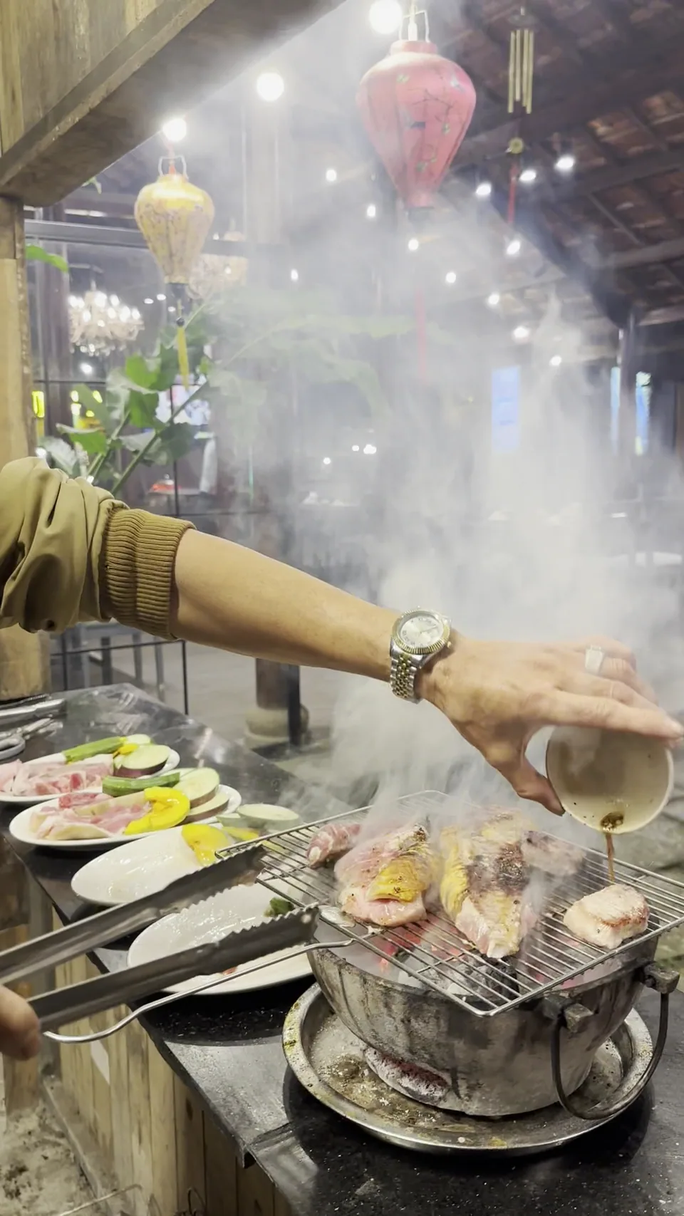 Khoảnh khắc rưới nước sốt lên đĩa bò tơ đang nướng tỏa khói thơm trên bếp than tại Bách Tùng An.