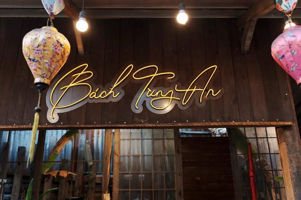 Bảng hiệu neon vàng "Bách Tùng An" treo giữa hai chiếc đèn lồng lụa Hội An ngay cửa quán.